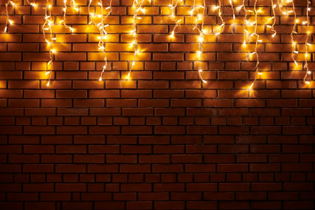 Yellow lights garlands hanging from red brick wall at evening, beautiful christmas house decoration